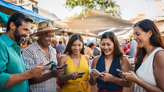 A diverse group of people in a lively Latin American marketplace, using mobile phones to make digital payments. The image highlights the accessibility and inclusivity of digital payments across different age groups and demographics in the region.