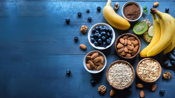 Health foods including bananas, blueberries, oats, almonds, and walnuts arranged on a dark blue table. These nutrient-rich foods are known for boosting energy, brain function, and overall health, perfect for entrepreneurs looking to maximize performance.