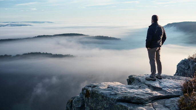 An individual stands on the edge of a cliff, looking out over a misty, fog-covered landscape, symbolizing an entrepreneur stepping into the unknown and embracing new opportunities.