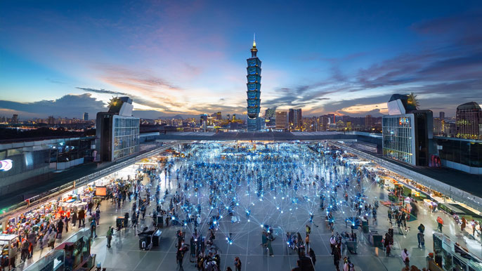 An aerial view of COMPUTEX TAIPEI with a vibrant trade show floor, illuminated digital connections, and the iconic Taipei 101 tower in the background, symbolizing global technology innovation.