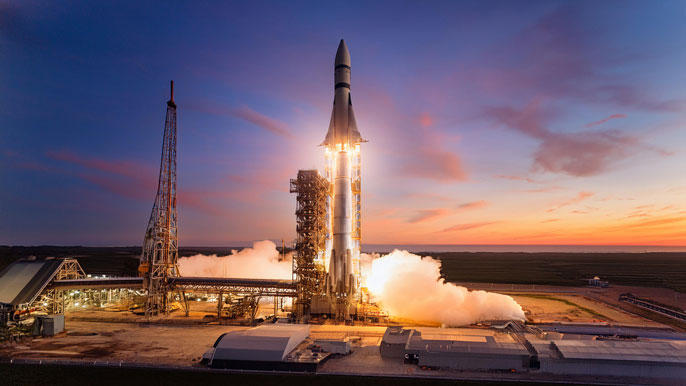 A rocket on a launch platform at sunset with complex structures and steam clouds.