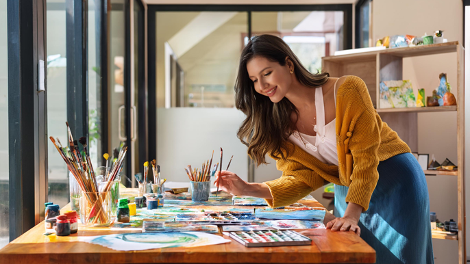 An artist painting in a bright studio, surrounded by brushes, paint, and vibrant artwork, symbolizing creativity, vision, and precision, similar to the entrepreneurial process of building a business.