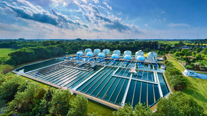 A large water purification facility with advanced filtration systems and clear water pools, surrounded by green fields and trees. The image highlights the role of environmental technology in clean water management and sustainability.