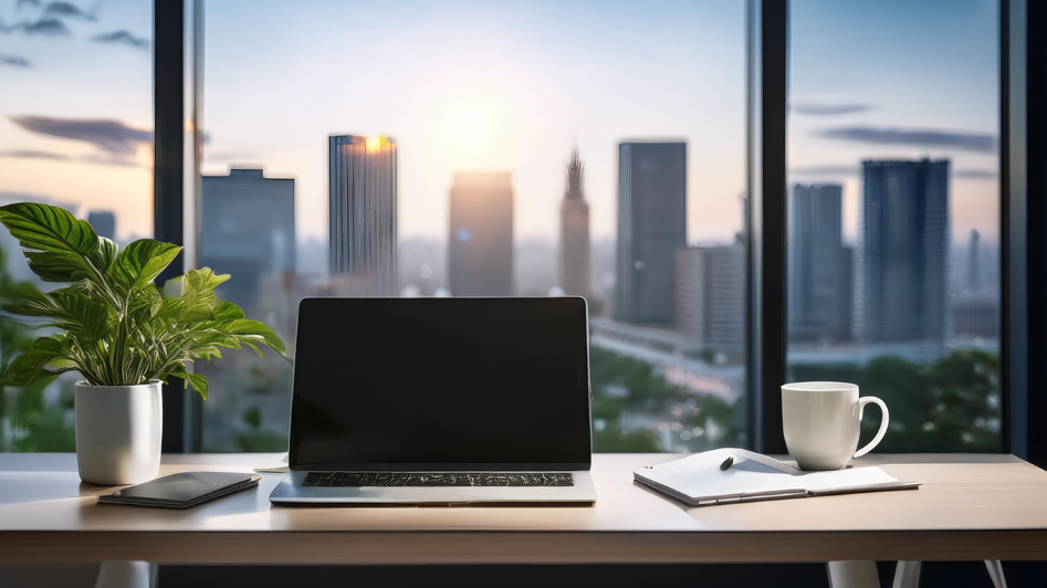 Modern workspace with a laptop, coffee cup, notebook, and plant on a clean desk, with a city skyline in the background.