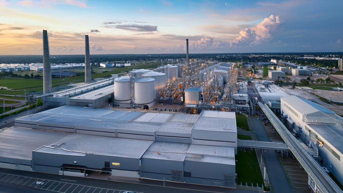 A close-up aerial view of two large industrial factories located side by side, connected by infrastructure, symbolizing reduced transportation costs and improved efficiency through agglomeration economies.