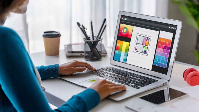 A graphic designer working on a laptop with digital design software open, displaying colorful logo and layout designs, symbolizing a home-based graphic design business.