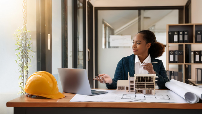 An architect working at a desk with blueprints, a model building, and a laptop, symbolizing precision, planning, and vision, representing the connection between architecture and entrepreneurship in building a successful business.