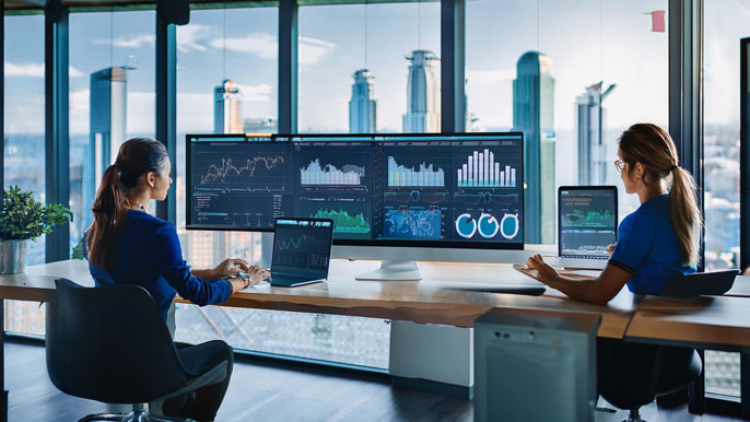 Two professionals in a modern office viewing an ERP dashboard with real-time data and charts on large screens, with a city skyline in the background.