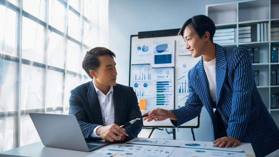 A business mentor guiding a startup founder by reviewing growth charts and offering strategic advice, symbolizing the benefits of mentorship for startup success.